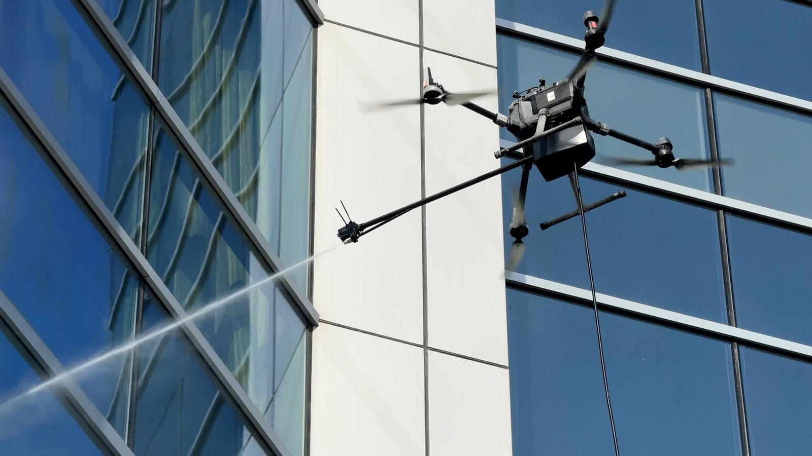 Dron z lancą ciśnieniową myjący szklaną fasadę biurowca